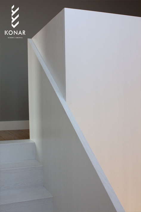 Minimalistyczne schody białe zabudowane ścianą również w białym kolorze. Schody idealnie komponują się z białymi ścianami.